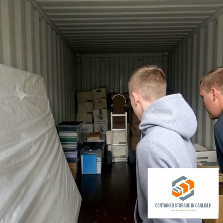 Two boys looking into a shipping container filled with boxes and furniture.